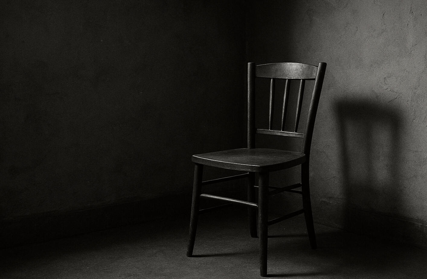 A black and white image of a solitary chair casting a long shadow against a textured wall.